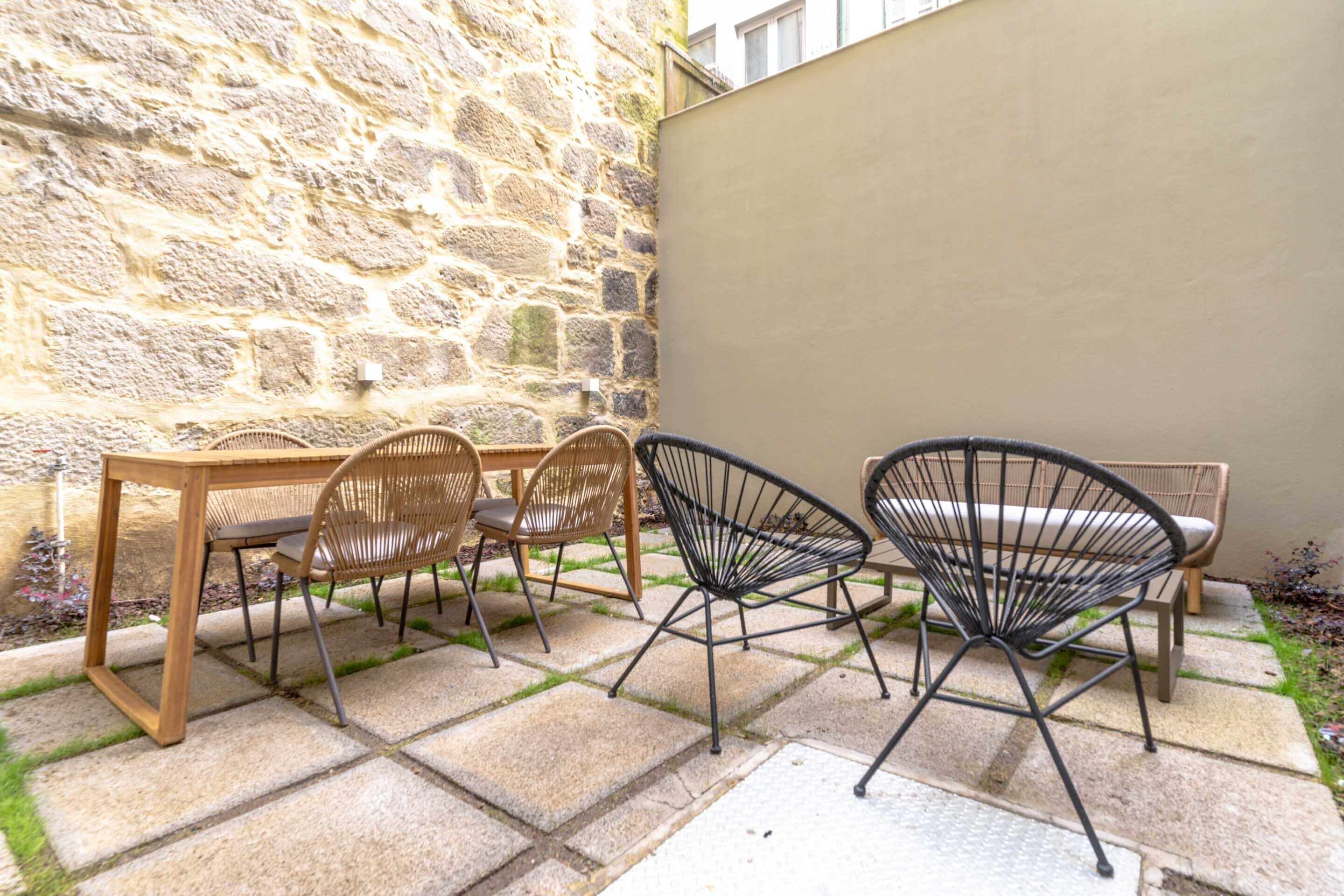 Un espace patio comprenant une table en pierre et quatre chaises, dont une avec un dossier en osier tressé et trois avec des structures en métal.