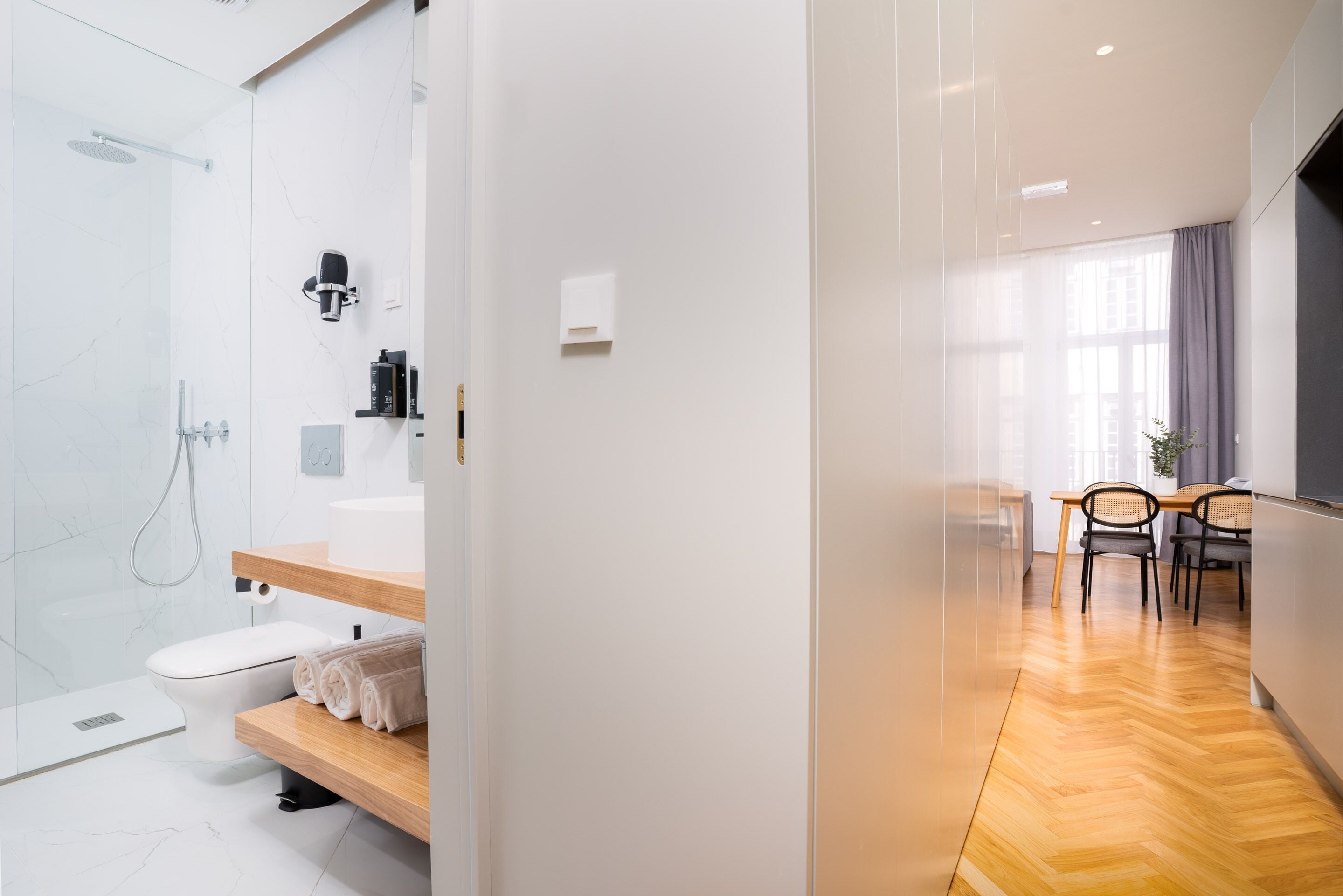 Un baño moderno con cabina de ducha de vidrio, accesorios blancos y un banco de madera.