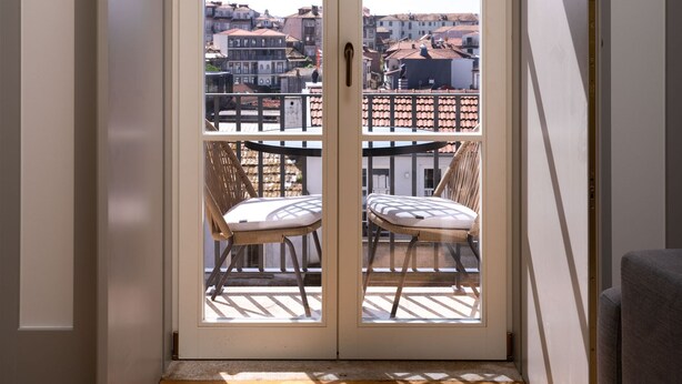 A room with a sliding glass door leading to an outdoor balcony with two wicker chairs. - Limehome Porto Rua 31 de Janeiro (Porto)