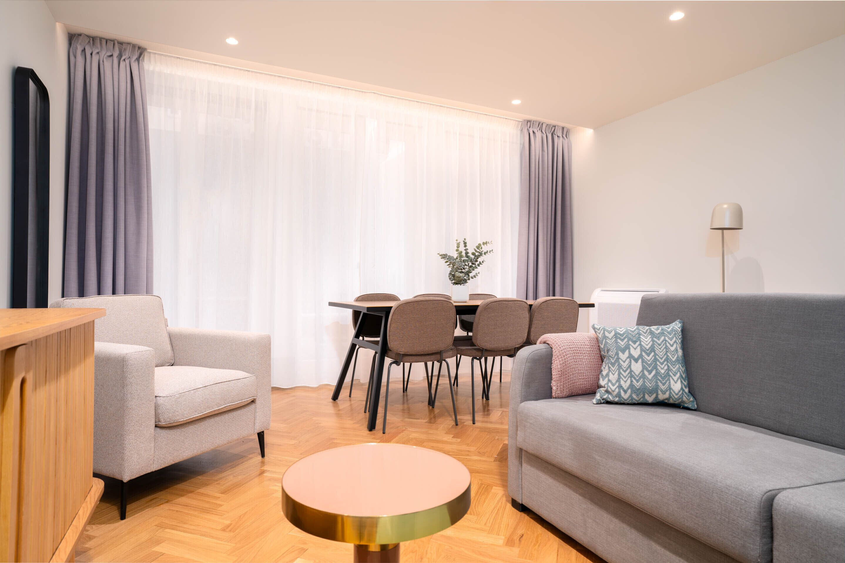 A modern living room with a grey sofa, a round coffee table, and a dining area with a table and chairs.