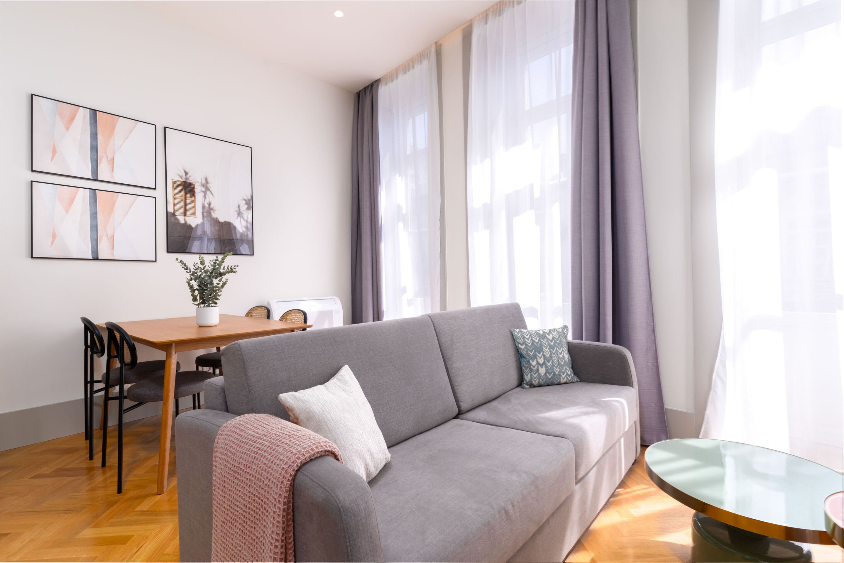 A modern living room with a grey sofa, a dining table with chairs, and artwork on the wall.