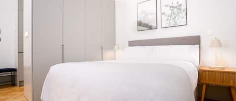 Quarto com uma cama grande, uma mesa de cabeceira com abajur e duas fotografias emolduradas na parede.