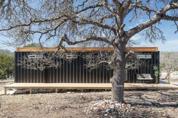 Un bâtiment moderne et minimaliste, doté d’une terrasse en bois et d’un banc, entouré d’un paysage aride et rocheux.