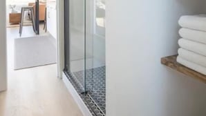 Un baño moderno con cabina de ducha de vidrio, un lavamanos blanco y un estante de madera con toallas dobladas.