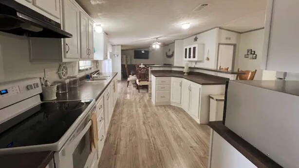Une cuisine moderne avec des meubles blancs, une plaque de cuisson noire et un plancher en bois.