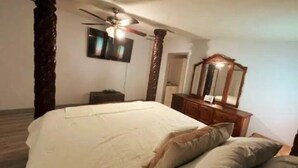 Une chambre à coucher avec un grand lit, un ventilateur de plafond, une commode en bois et un miroir.