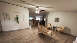 Un salon spacieux doté d’un plancher en bois, d’un canapé, de deux fauteuils, d’une petite table et d’un ventilateur de plafond.