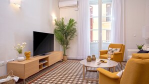 Un salon moderne doté d’un téléviseur à écran plat, d’une plante en pot, d’une table à manger avec des chaises et d’une grande fenêtre agrémentée de rideaux.