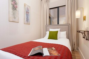 A hotel room with a bed, a window with curtains, a wall-mounted light fixture, and two paintings. - Exclusive apartment near Cathedral. Rodrigo Caro II (Seville)