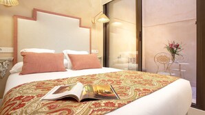Hotellihuone, jossa on suuri sänky, sängyllä lehti, pieni pöytä maljakko täynnä kukkia ja ikkunasta avautuva näkymä kaupunkiin.