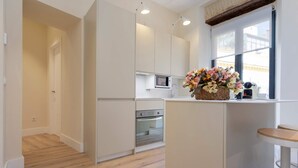 A modern kitchen with white cabinetry, a microwave, and an oven. There's a small island with a vase of flowers. - Genteel Home Rodrigo Caro Terrace III (Seville)