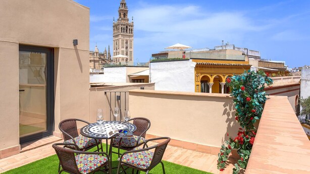 A rooftop terrace with a table and chairs, a view of a historic tower, and a building with arches. - Genteel Home Rodrigo Caro Terrace III (Seville)