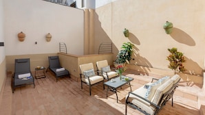 A sunlit patio with four lounge chairs, a small table, and a potted plant.