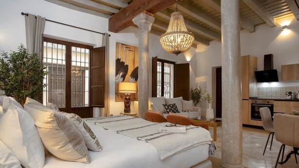 A bedroom with a large bed, a chandelier, and a view of the kitchen. - Genteel Home Horno Marina 1 (Granada)