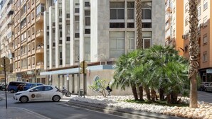 Un edificio moderno con una fachada geométrica distintiva, palmeras y un cielo despejado.