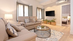 Een moderne woonkamer met een bank, fauteuils, een salontafel en een flatscreen televisie aan de muur.