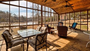 Un espacio exterior techado con una mesa y sillas, ventanas amplias y vistas al exterior.