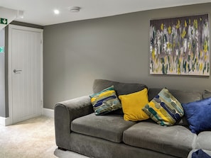 A grey sofa with colorful cushions, a white door, and a wall with a textured abstract painting. - Doodles Holiday Home (Eyemouth)