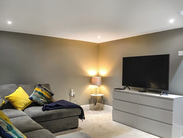 A modern living room with a grey sofa, a flat-screen TV, and a small side table with a lamp.
