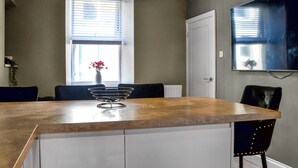 A modern kitchen with a wooden countertop, a white cabinet, a black chair, and a vase with flowers on the window sill. - Doodles Holiday Home (Eyemouth)