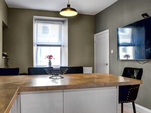 A modern kitchen with a wooden countertop, a white cabinet, a black chair, and a vase with flowers on the window sill.