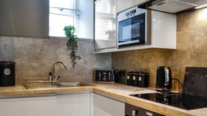 A modern kitchen with a built-in microwave, a toaster, and a stove. - Doodles Holiday Home (Eyemouth)