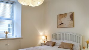A bedroom with a bed, bedside tables, a window with blinds, a wall-mounted artwork, and a ceiling light fixture. - Doodles Holiday Home (Eyemouth)