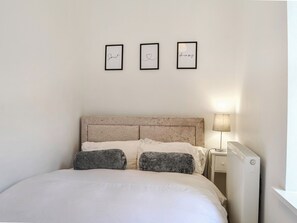 A bedroom with a bed, a nightstand, a lamp, and three framed items on the wall. - Doodles Holiday Home (Eyemouth)