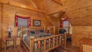 A log cabin bedroom with a wooden bed, two nightstands, a chair, and a window with blinds. - 5-Bedroom Mountain Lodge with Views and Games (PIGEON FORGE)
