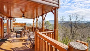 A wooden deck with a table and chairs, a ceiling fan, and a view of the surrounding landscape. - 5-Bedroom Mountain Lodge with Views and Games (PIGEON FORGE)