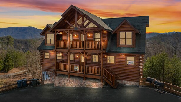 A log cabin with a balcony, stone foundation, and a sign indicating a room rate of $275. - 5-Bedroom Mountain Lodge with Views and Games (PIGEON FORGE)