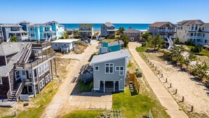 A coastal residential area with multi-story houses, a central pathway, and a beach in the background. - Oceanside Cottage Steps from the Beach! The Gray Sandcastle! (Nags Head)