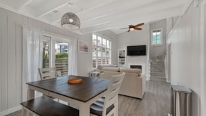 A dining area with a wooden table and chairs, a ceiling fan, and a TV mounted on the wall. - Oceanside Cottage Steps from the Beach! The Gray Sandcastle! (Nags Head)