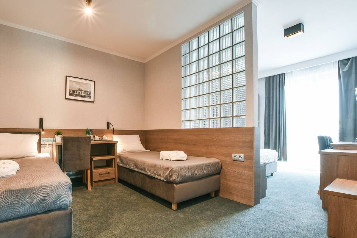 A hotel room with two beds, a desk, a chair, a large window, and a picture on the wall.