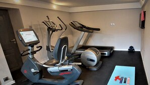 A gym with an elliptical machine, a treadmill, and a rowing machine. There is a blue mat on the floor and a small table with dumbbells and resistance bands. - Willa Marcel Park (Busko-Zdroj)