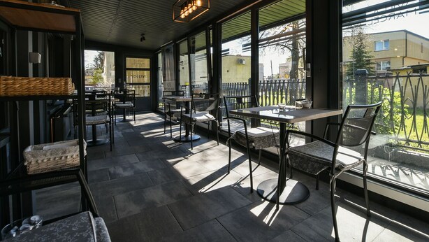 An outdoor café with tables and chairs, large windows, and a metal ceiling. - Willa Marcel Park (Busko-Zdroj)