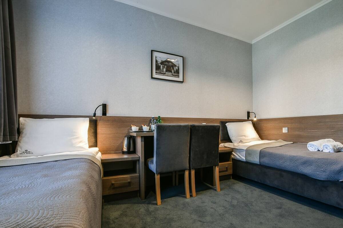 A hotel room with two beds, a desk, a chair, a small table, and a picture on the wall.