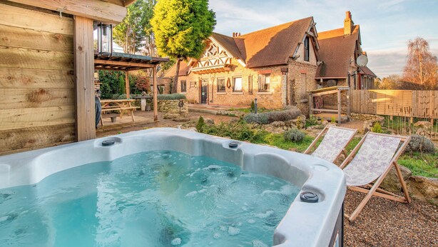 Un jacuzzi en un patio trasero con terraza de madera, pared de piedra y una casa con fachada de ladrillo.