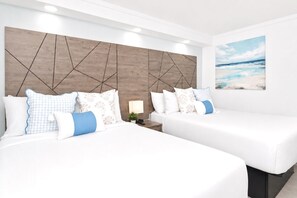 A hotel room with two beds, a wooden headboard, a nightstand, a lamp, and a beach view painting. - Fin's Inn & Suites  (Myrtle Beach)