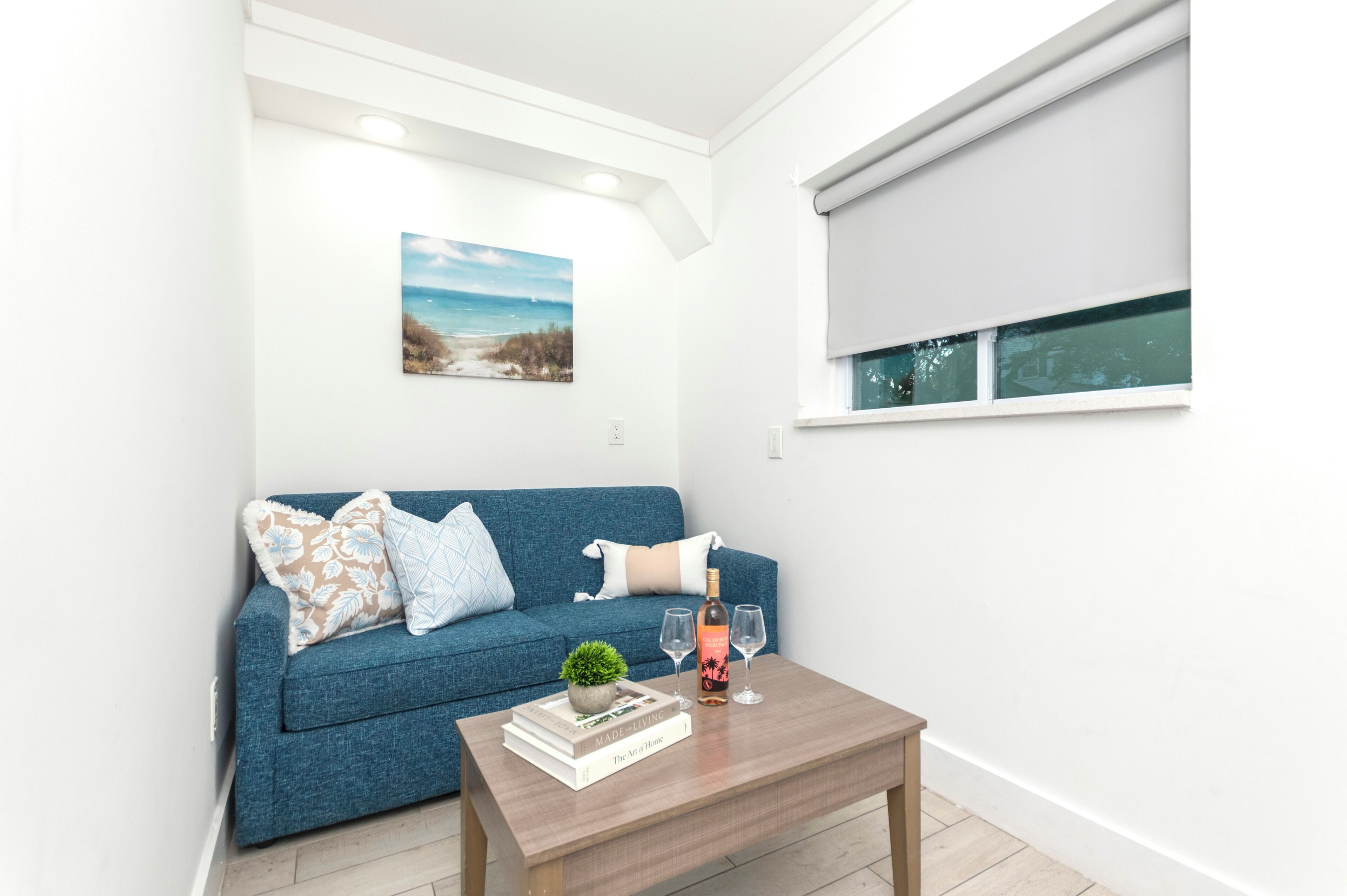 A modern living room with a blue sofa, a coffee table with books and a bottle, and a painting on the wall.