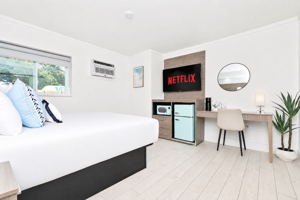 Una habitación de hotel moderna con cama, escritorio, televisión y una pequeña kitchenette.
