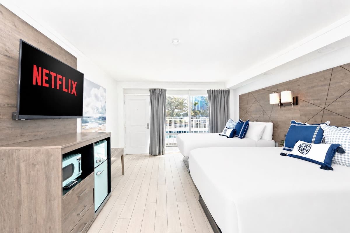 Habitación de hotel con una cama grande, un televisor montado en la pared, un escritorio con una computadora y vistas al exterior.