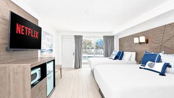 Quarto de hotel com uma cama grande, uma TV fixada na parede, uma escrivaninha com computador e vista para o exterior.