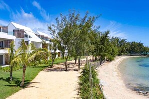 Une propriété située en bord de mer, avec des bâtiments blancs, un sentier sablonneux et une vue dégagée sur l’océan.