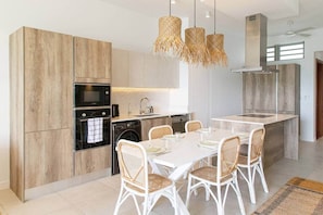 Eine moderne Küche mit Holzausstattung, einem eingebauten Backofen, einem Geschirrspüler und einem Essbereich mit weißem Tisch und Korbstühlen.
