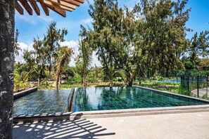 A swimming pool with a stone border, surrounded by trees and a clear sky.