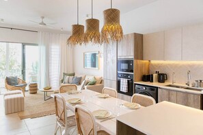 A modern kitchen with a dining area, large windows, and a ceiling fan.