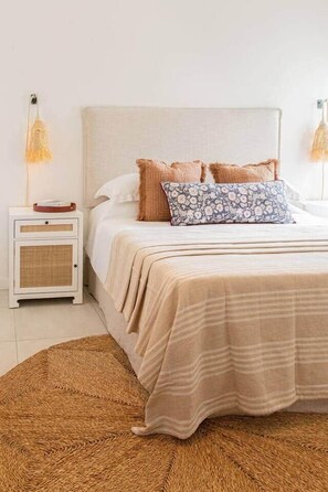 Un lit avec une tête de lit de couleur beige, un coussin à motifs et un tapis tissé.