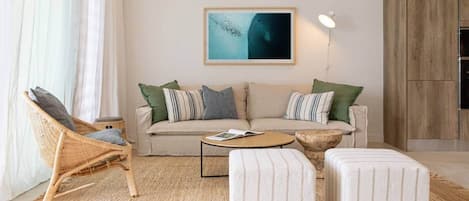 Un salon comprenant un canapé, deux poufs, une table basse, un fauteuil en osier et une lampe fixée au mur.