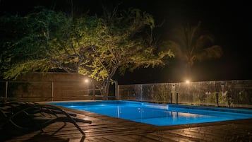 Piscina à noite, com árvores ao redor e um deck de madeira.